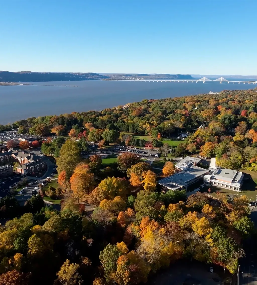 Aerial view of campus buildings among autumn trees on a hillside above a wide river