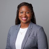 Head and shoulders professional portrait of person in suit jacket, smiling and looking at camera.