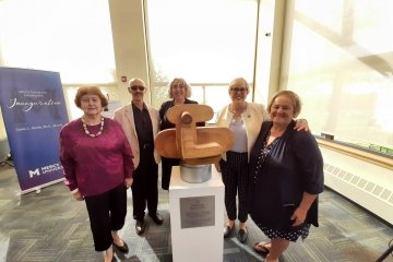 Artist and sculpture surrounded by Mercy officials and alumni