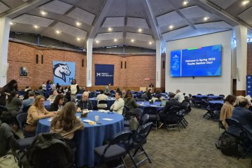 Photo of multiple round tables with blue tablecloths surrounded by people at Faculty Seminar Day, Spring 2026.