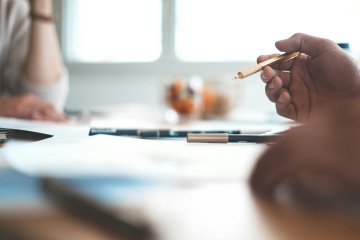 Shallow focus photo of person holding pen, with another person seated across the table.