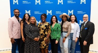 Organizers Mercy University and The Bronx Community Foundation representatives pose with some of the day's panelists in front of Mercy University step and repeat banner in the background