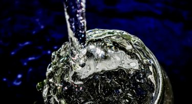 Photo of water pouring into a clear glass with a dark blue background