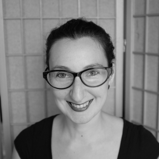 Black and white image of Sara Martucci wearing glasses and smiling. 