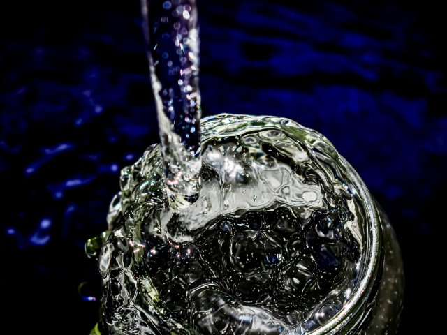 Photo of water pouring into a clear glass with a dark blue background