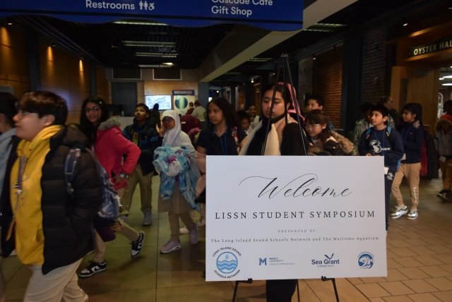 K-12 students at The Maritime Aquarium walking past poster welcoming them to the Long Island Sound Symposium