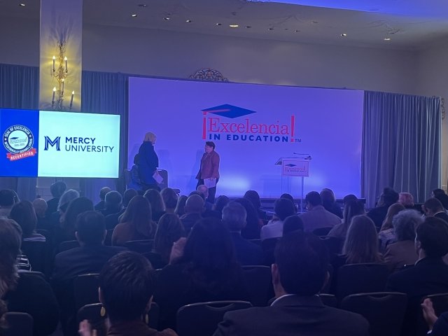 Mercy University president walks to the stage to receive Seal of Excelencia recertification